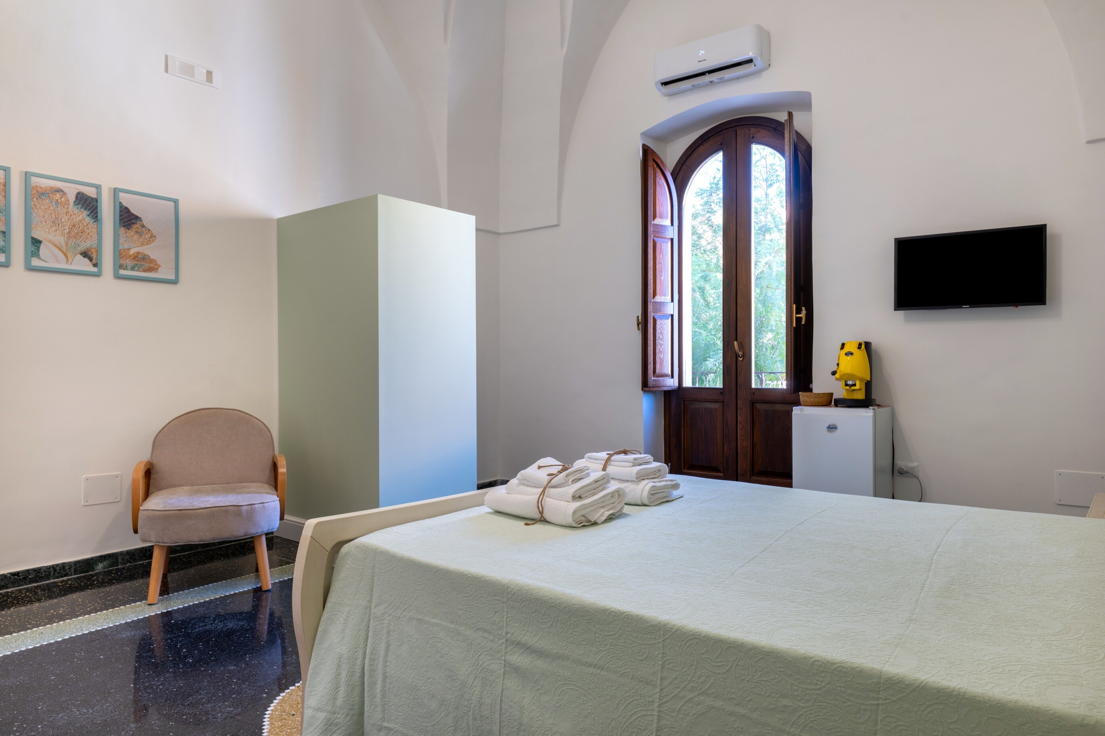 A hotel room with a bed, a chair, a desk with a computer, and a TV.