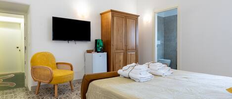 Una habitación de hotel con cama, televisión, armario, silla y refrigerador pequeño.