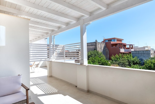 A balcony with a white railing, a wicker sofa, and a view of buildings and greenery.