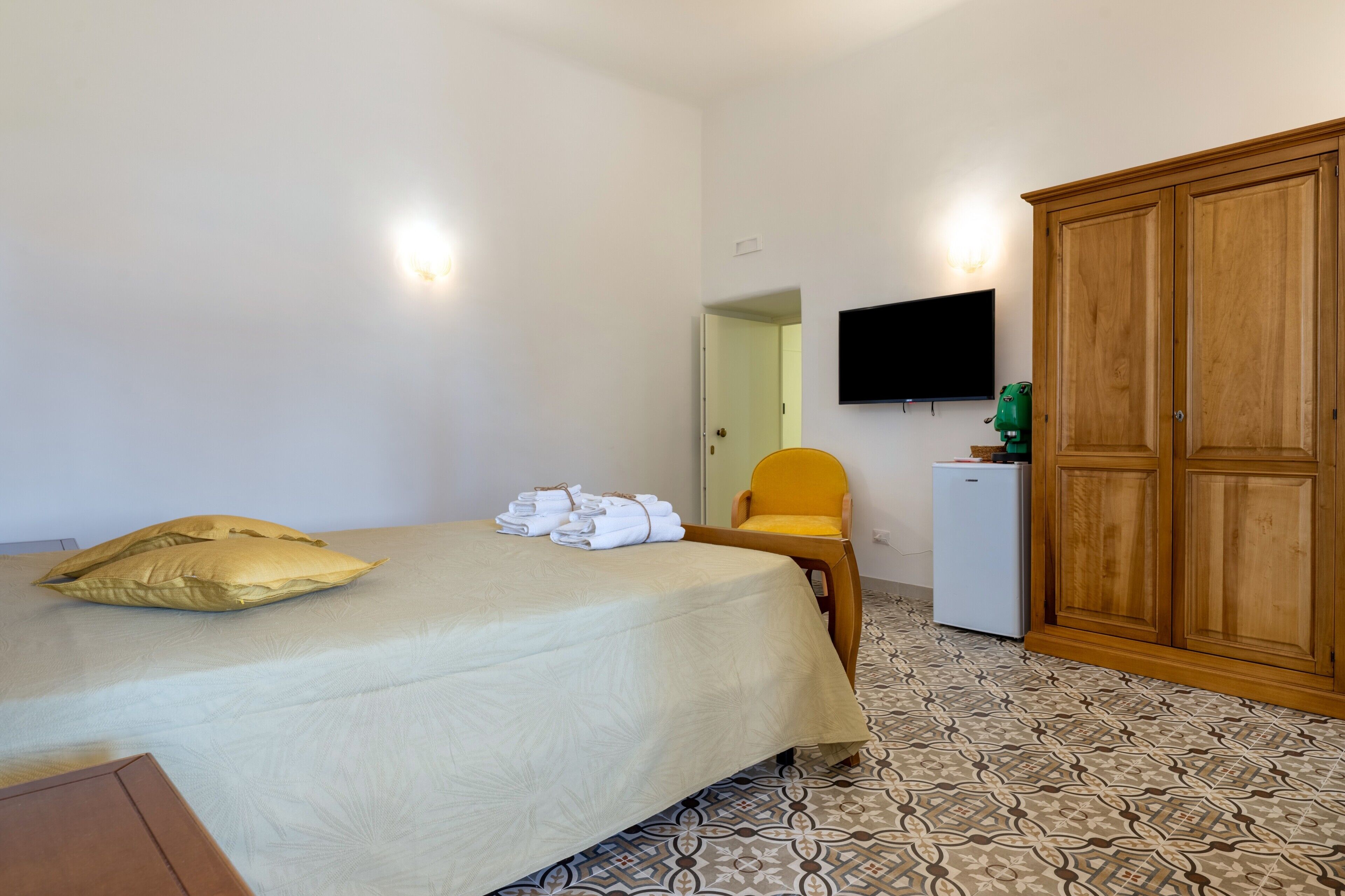 Una camera d'albergo con un letto, una televisione, un armadio, una scrivania e una sedia.