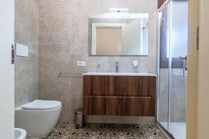 A bathroom with a toilet, a wooden vanity with a mirror, and a shower area.