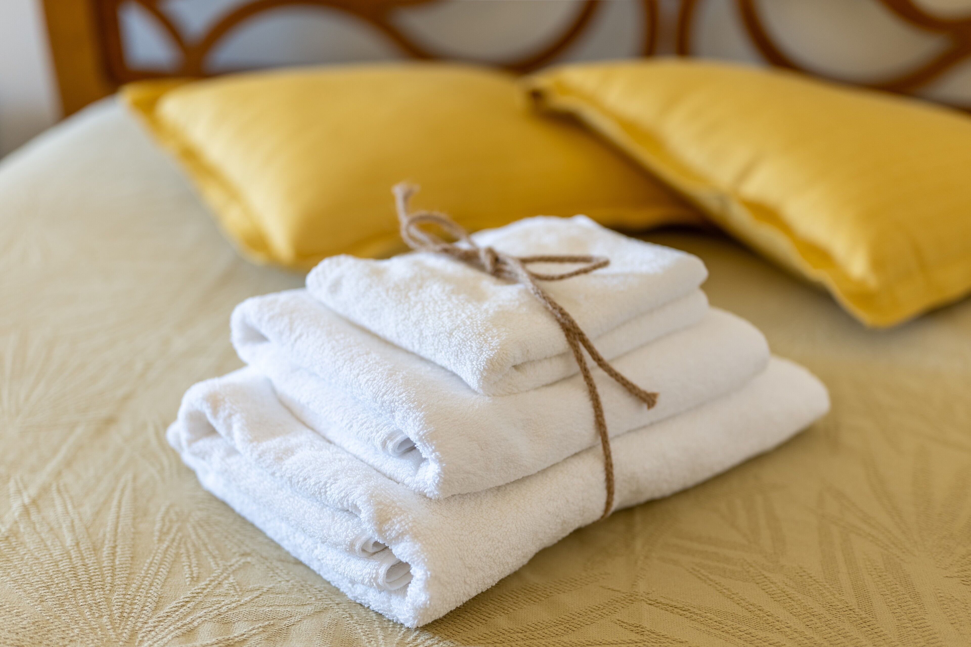 A bed with a neatly folded white towel and a brown string tied around it, placed on a textured bedspread.