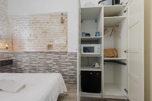 Una habitación con una cama, un armario blanco, un microondas y un refrigerador pequeño.
