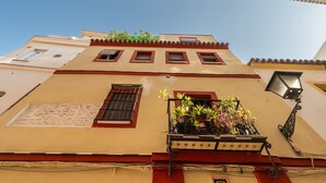 Un edificio con balcón, plantas en macetas, una ventana con reja y una lámpara fijada a la pared.