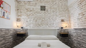 Un dormitorio con pared de piedra, una cama con ropa de cama blanca, dos mesitas de noche y una pequeña baldosa decorativa en la pared.