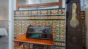 Una habitación con pared de azulejos, un expositor de madera, un reloj grande y una mesa con mantel blanco.