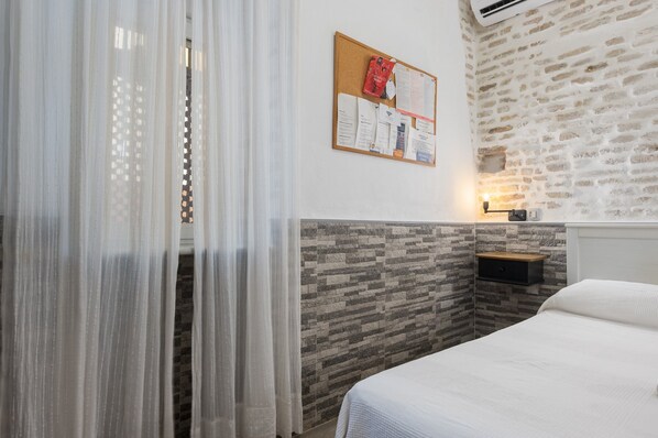 A bedroom with a bed, a corkboard with papers, a nightstand, and a stone-patterned wall.