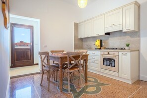 A kitchen with white cabinets, a stove, and a dining area with wooden chairs. - Apartment 'Primo Piano - Mini' with Private Garden, Wi-Fi and Air Conditioning (Pulsano)