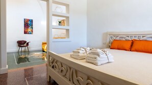Habitación de hotel con cama, una silla, estante con toallas y un cuadro en la pared.
