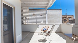 Un balcón con una silla, una ventana con persianas y vistas a edificios.