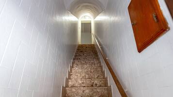 Een trap met witte muren en een houten leuning die naar een deur boven leidt.