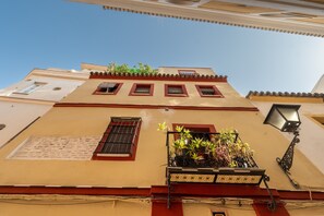 A building with a balcony with potted plants, a window with a metal grille, and a wall-mounted light fixture. - Apartment 'Doble Superior' with Wi-Fi and Air Conditioning (Sevilla)