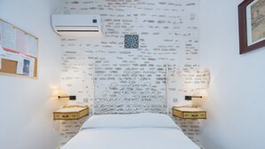 A narrow hotel room with a single bed, a decorative headboard, two bedside tables with lamps, an air conditioning unit, and a corkboard with notices. - Apartment 'Doble Superior' with Wi-Fi and Air Conditioning (Sevilla)