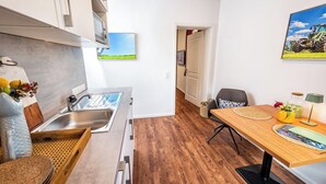 Ett kompakt kök med en diskho, trägolv, en matplats med bord och stolar samt utsikt över en grön äng genom en öppen dörr.