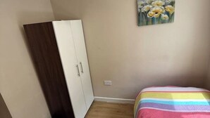 Un dormitorio con un armario, una cama con una manta a rayas de arcoíris y un cuadro floral en la pared.