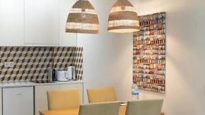 A dining area with a wooden table and chairs, two hanging pendant lights, a kitchen with a geometric backsplash, and a bookshelf on the wall. - Oporto Riverside Rooftop (Porto)
