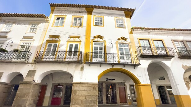 Un edificio histórico con un arco central, varios balcones con barandillas de hierro forjado y una entrada en la planta baja.