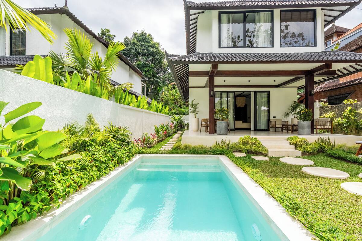 Une maison moderne dotée d’une piscine, entourée d’une végétation luxuriante et agrémentée d’un patio.