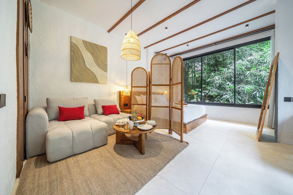 Un salon moderne avec un canapé, une table basse et une grande fenêtre donnant sur un paysage verdoyant.