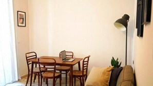 A living room with a brown sofa, a wooden dining table with four chairs, a laptop on the table, and a floor lamp.
