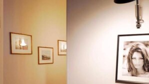 A hallway with framed pictures on the wall, a desk with a lamp, and a patterned carpet.