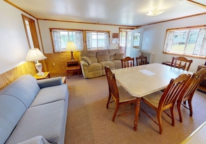 Un acogedor interior de cabaña con una mesa de comedor, sillas, un sofá y una lámpara.