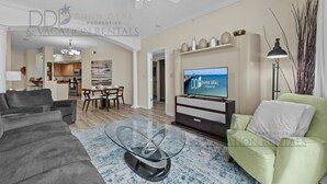 Een moderne woonkamer met een flatscreen-tv, een plafondventilator en een eethoek met een tafel en stoelen.