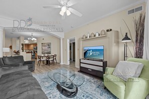 A modern living room with a television, a dining area, and a green armchair. - Legacy Tower II 1106 | Stunning Coastal Views! (Gulfport)