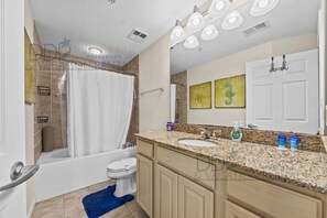 Un baño con bañera, inodoro y lavamanos. Hay luces en el techo, un perchero y un espejo.