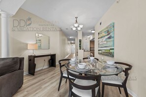 Comedor con una mesa de vidrio preparada para cuatro, un sofá y una obra de arte colgada en la pared.