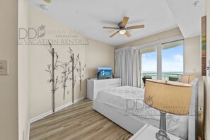 Un dormitorio moderno con cama, ventilador de techo, televisor y vista al océano.