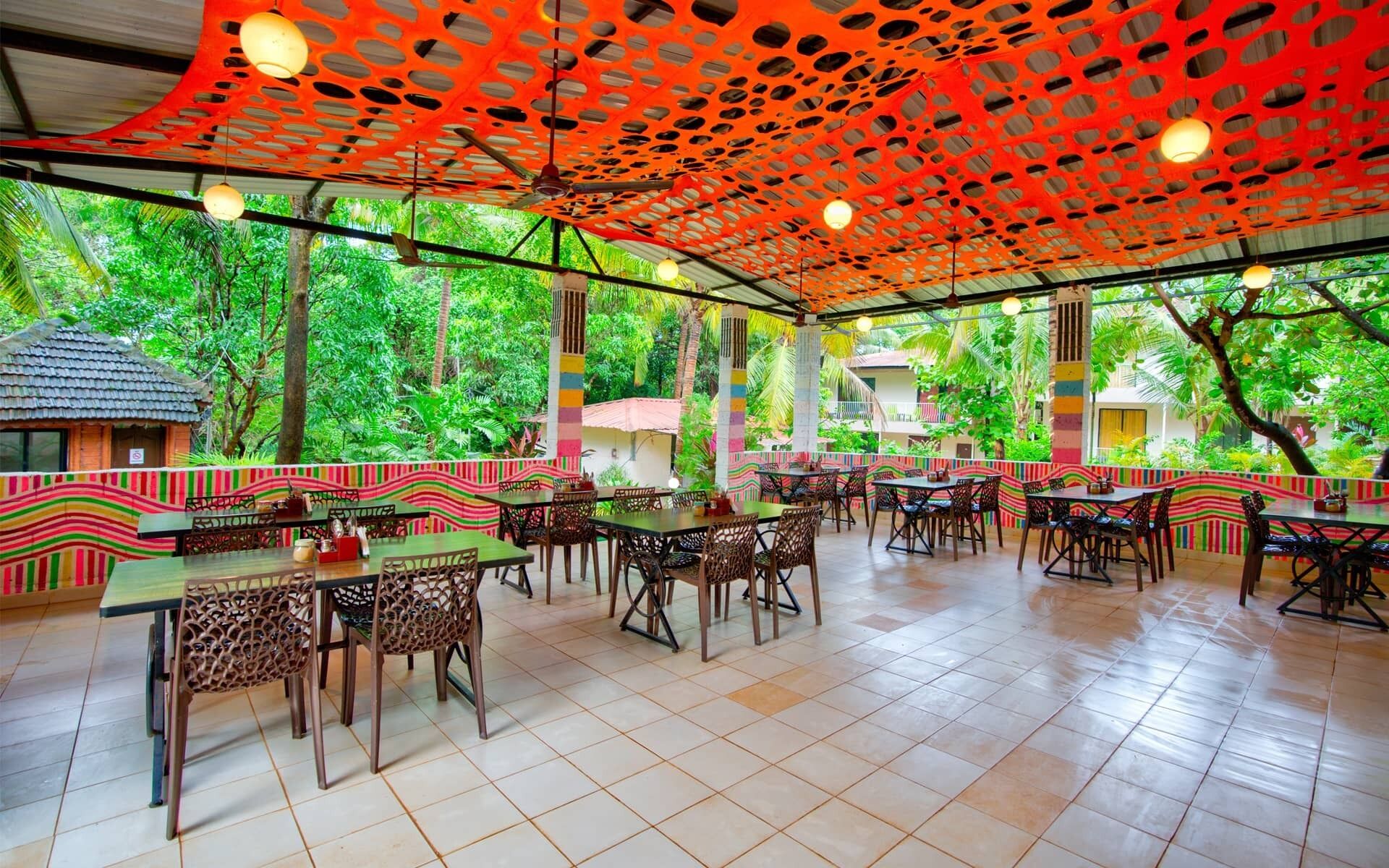 An outdoor restaurant with tables and chairs, surrounded by lush greenery.
