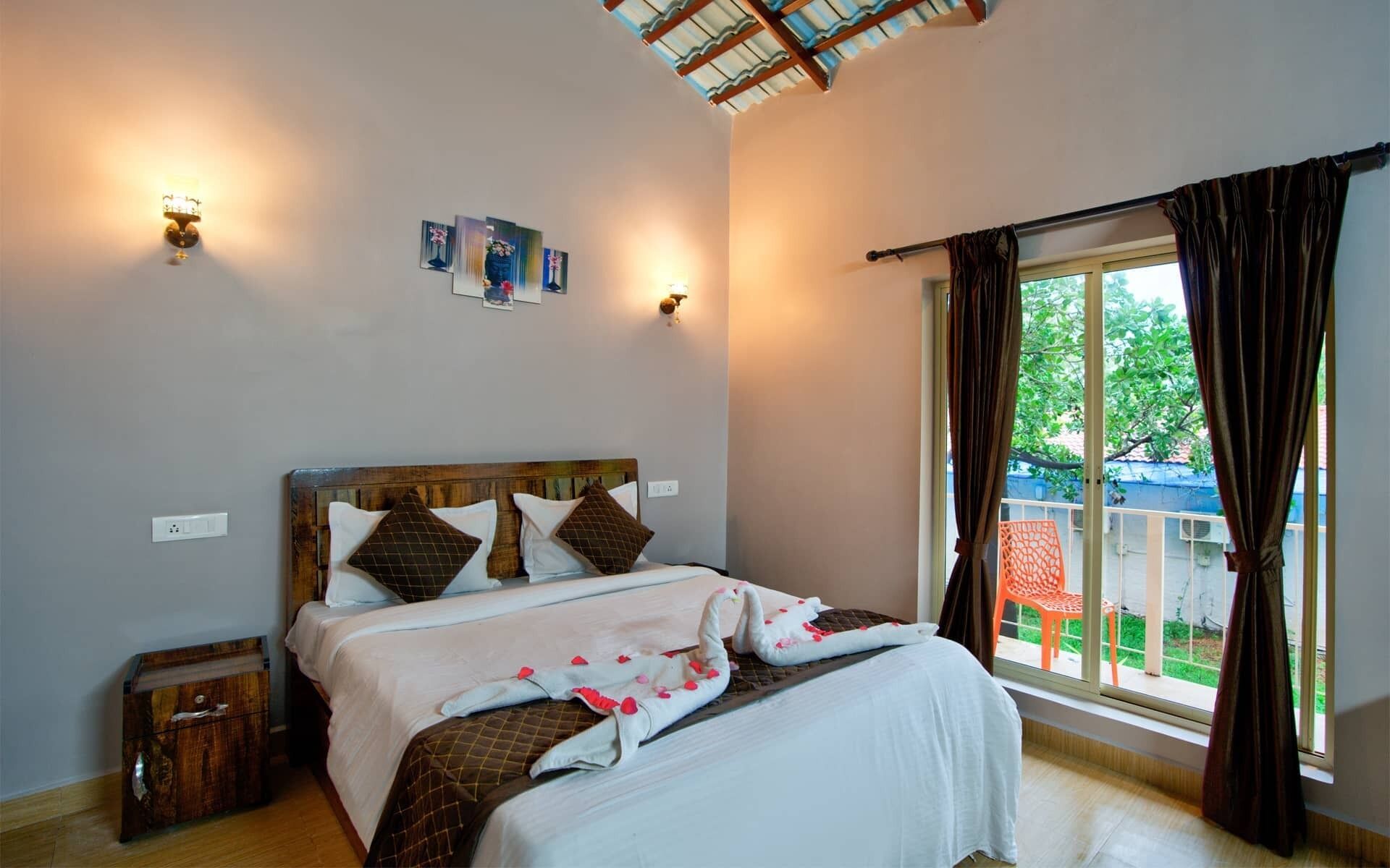 Une chambre à coucher avec une tête de lit en bois, un lit avec une literie blanche et marron, deux lampes fixées au mur et une fenêtre avec des rideaux.