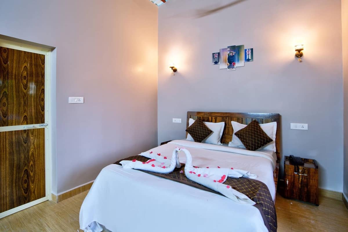 A neatly made bed with a white comforter and decorative swan pillows, a wooden headboard, and a wall-mounted light fixture.