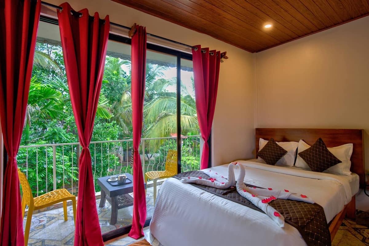 A hotel room with a large bed, a wooden headboard, and a balcony with red curtains.