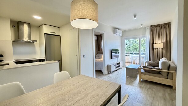 A modern kitchen with a dining area, a sofa, and a balcony with curtains.