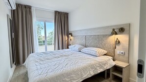 A bedroom with a bed, curtains, a window, and wall-mounted lighting.