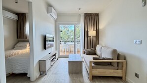A modern, well-lit room with a bed, a sofa, a TV, and a balcony with a table and chairs.