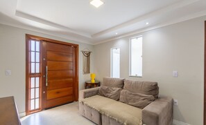 Un salon avec un canapé beige, une porte en bois et une petite table sur laquelle se trouve une lampe jaune.