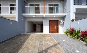Un edificio moderno con fachada gris, una puerta de madera y un balcón con barandilla de metal.