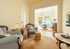 Una sala de estar con sofá, sillón, reposapiés y una mesa con un florero.