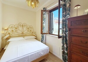 Une chambre à coucher avec un lit, une commode en bois, une fenêtre avec des rideaux et un luminaire au plafond.