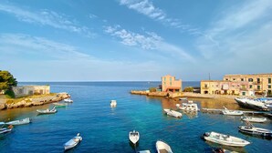 A coastal town with boats docked in a harbor, buildings along the shore, and a clear sky. - Solemar Sicilia - Palazzo Tiglio (Porticello)