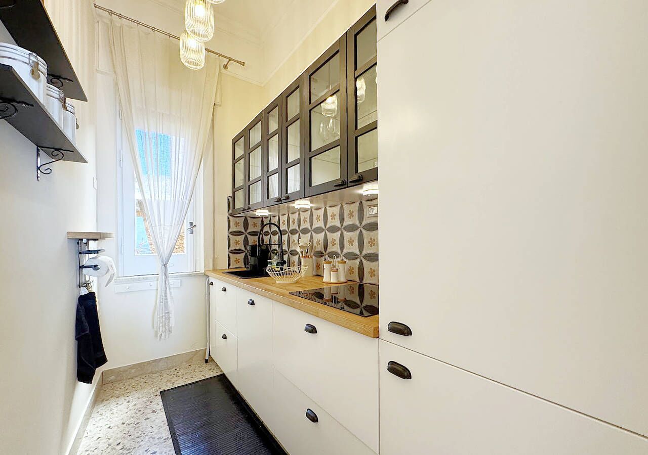 Une cuisine de taille réduite avec des meubles blancs, un plan de travail en bois et des carreaux décoratifs sur le mur derrière l’évier.