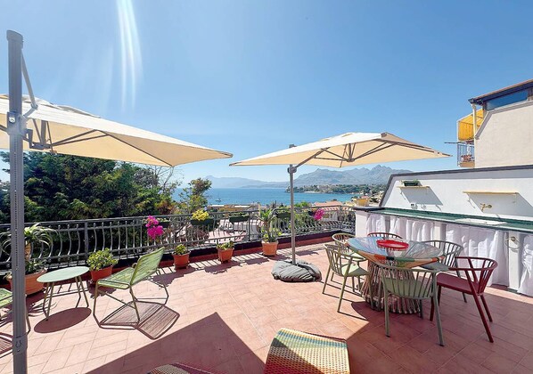 Une terrasse avec des sièges extérieurs, des plantes en pot et une vue sur la mer.