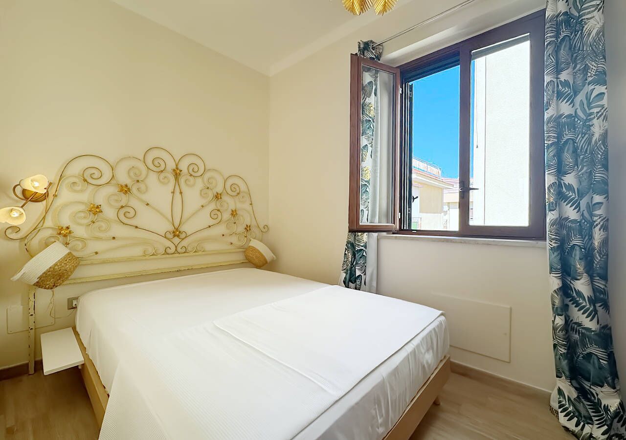 A bedroom with a bed, a headboard with a decorative design, a window with curtains, and a nightstand with a lamp.