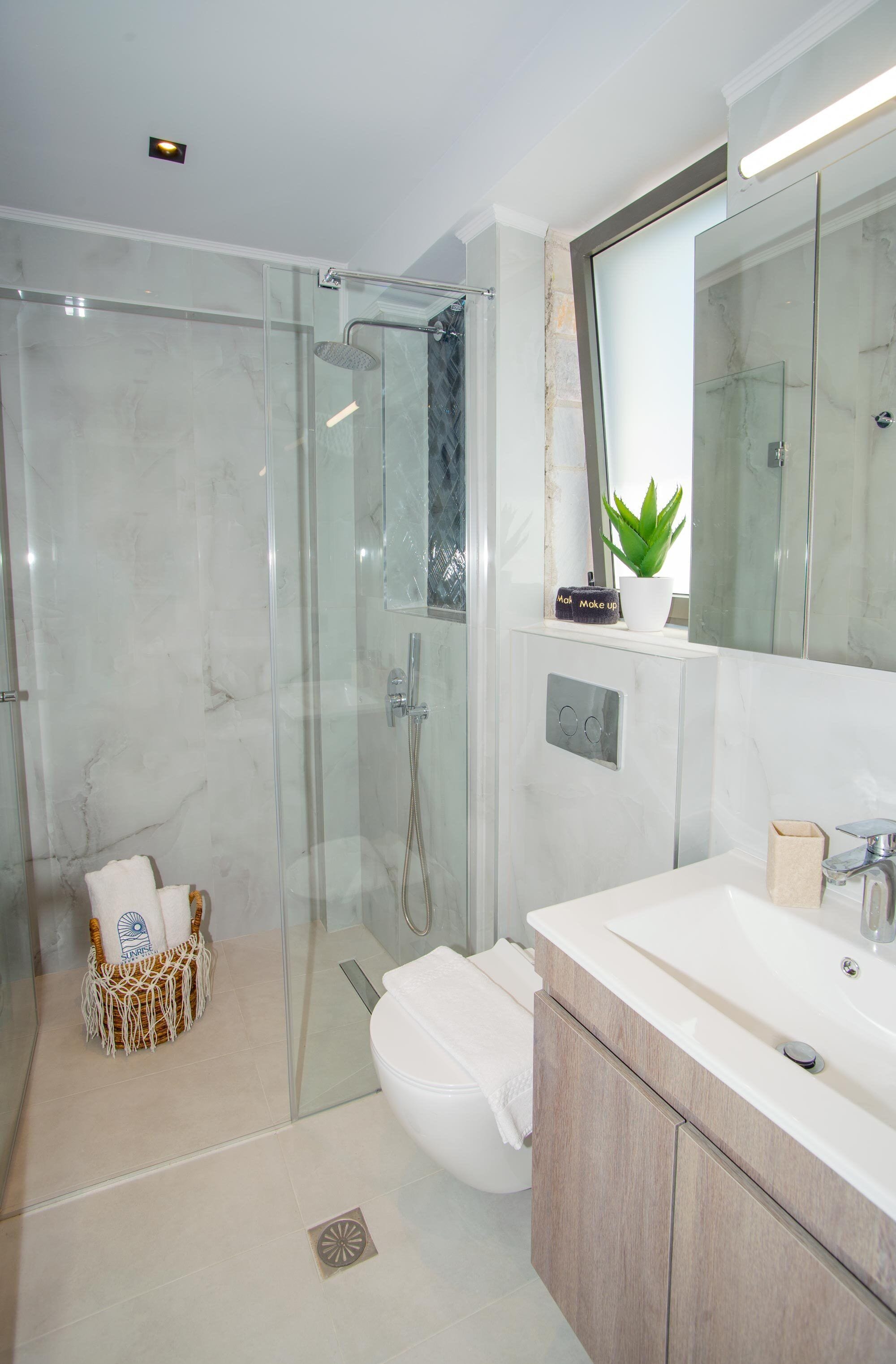 Une salle de bain moderne avec une douche à parois de verre, des toilettes blanches et un meuble-lavabo avec un miroir.
