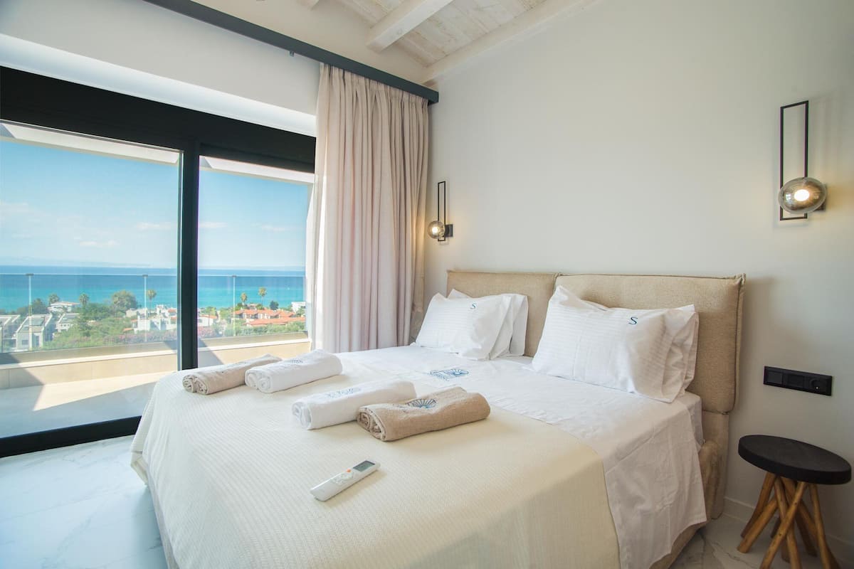 A hotel room with a large bed, a view of the sea, and a small table.