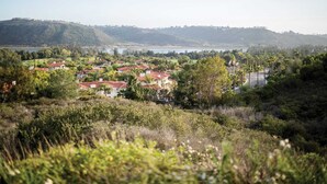 Un quartier résidentiel où les maisons se distinguent par leurs toits recouverts de tuiles rouges, le tout étant entouré d’une végétation luxuriante et avec des collines en arrière-plan.