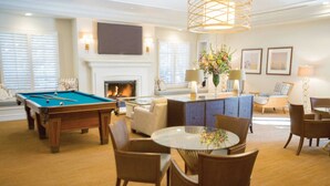 Un salon bien éclairé, équipé d’une table de billard, de sièges confortables, d’une cheminée et d’un téléviseur.